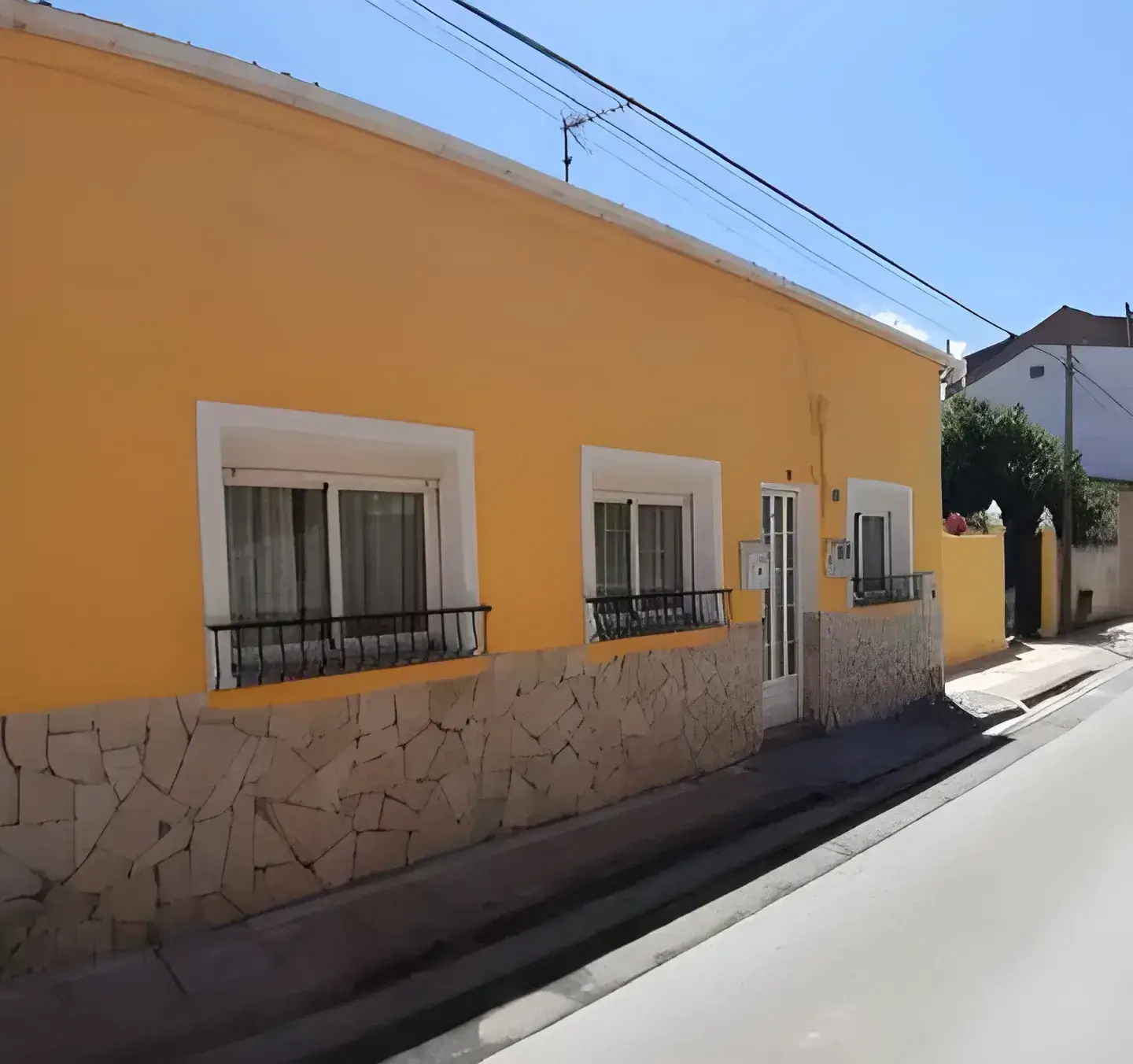 Los Pintores Marbella Fachada de casa tradicional pintada en color amarillo con zócalo de piedra